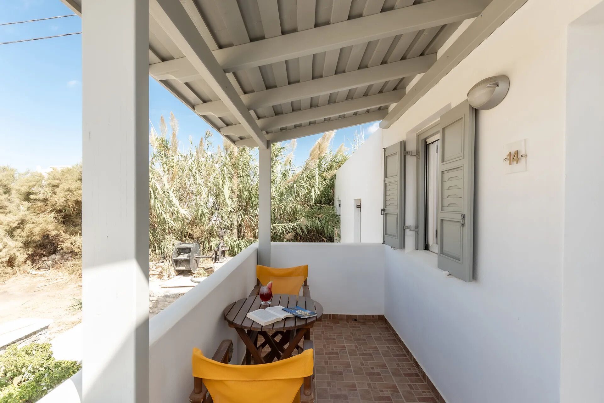 A covered balcony with a table and chairs, a door, and a view of a dry landscape.