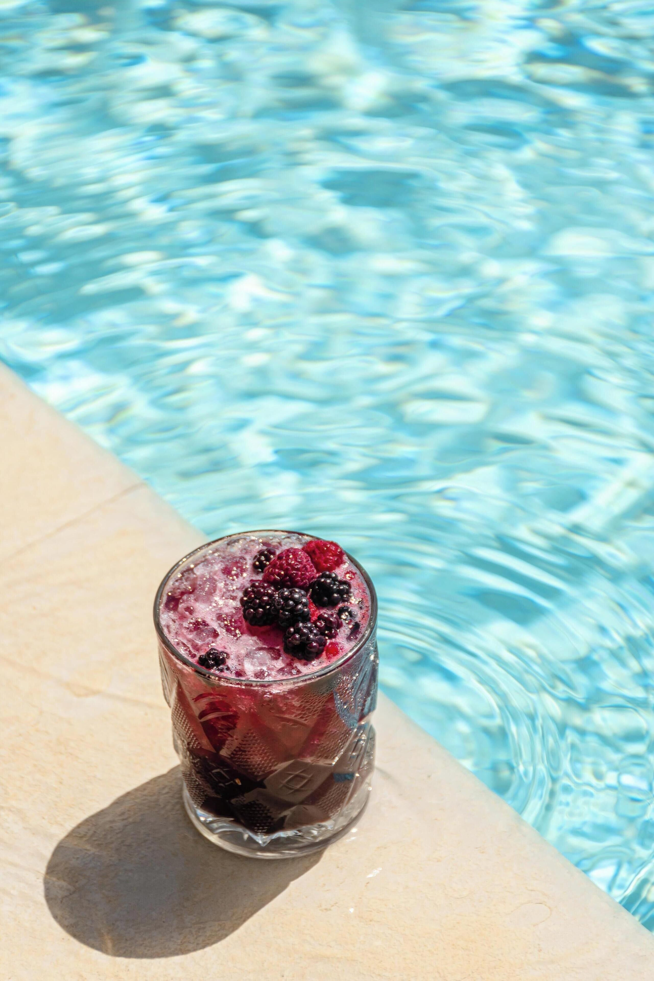 A glass of iced drink with berries on a poolside.