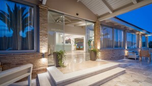 A modern hotel entrance with a glass facade, a brick exterior, and a patio area with outdoor seating. - Hotel Zakynthos  (Zakynthos)