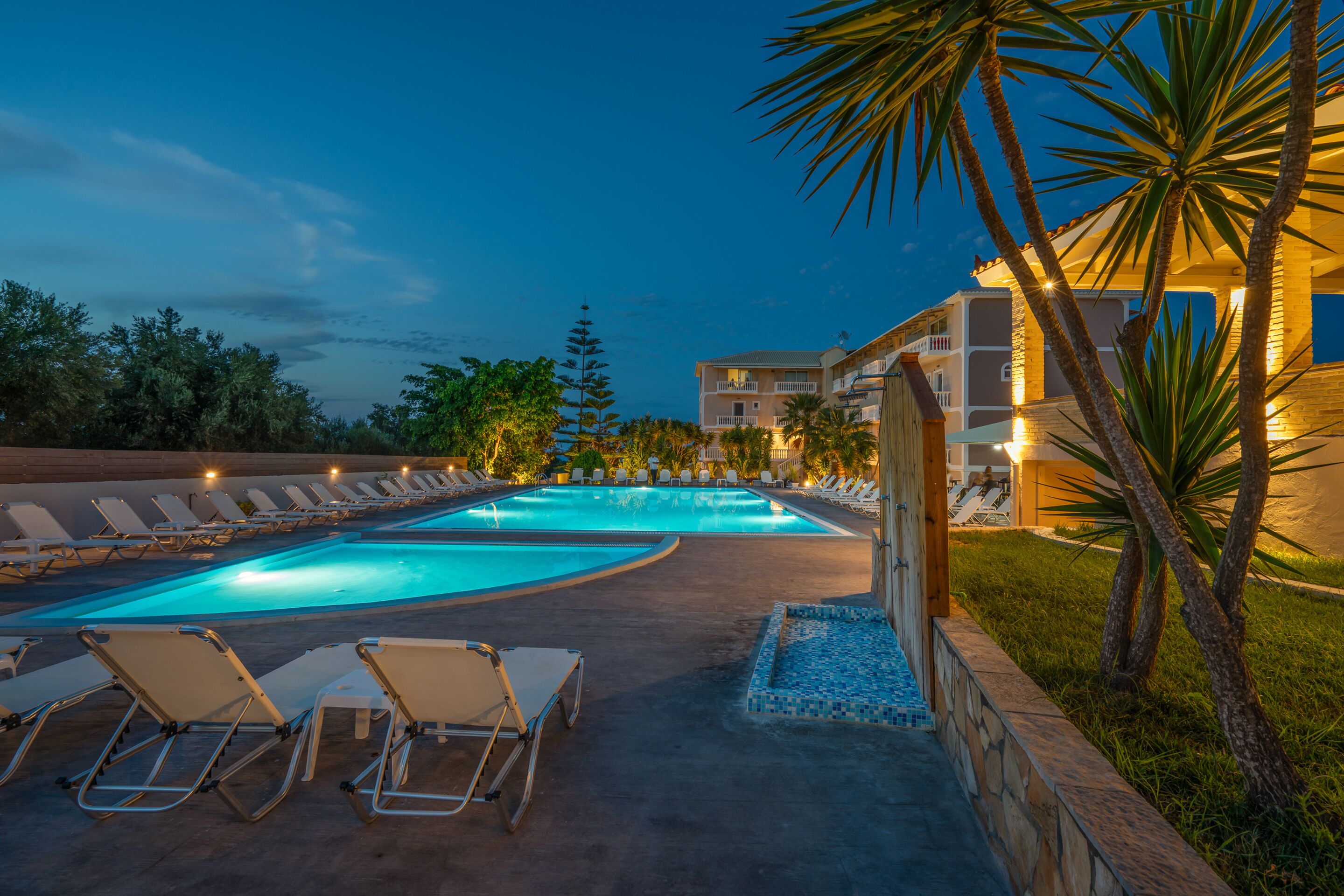 Zona de piscina con sillones de descanso y un edificio al fondo.