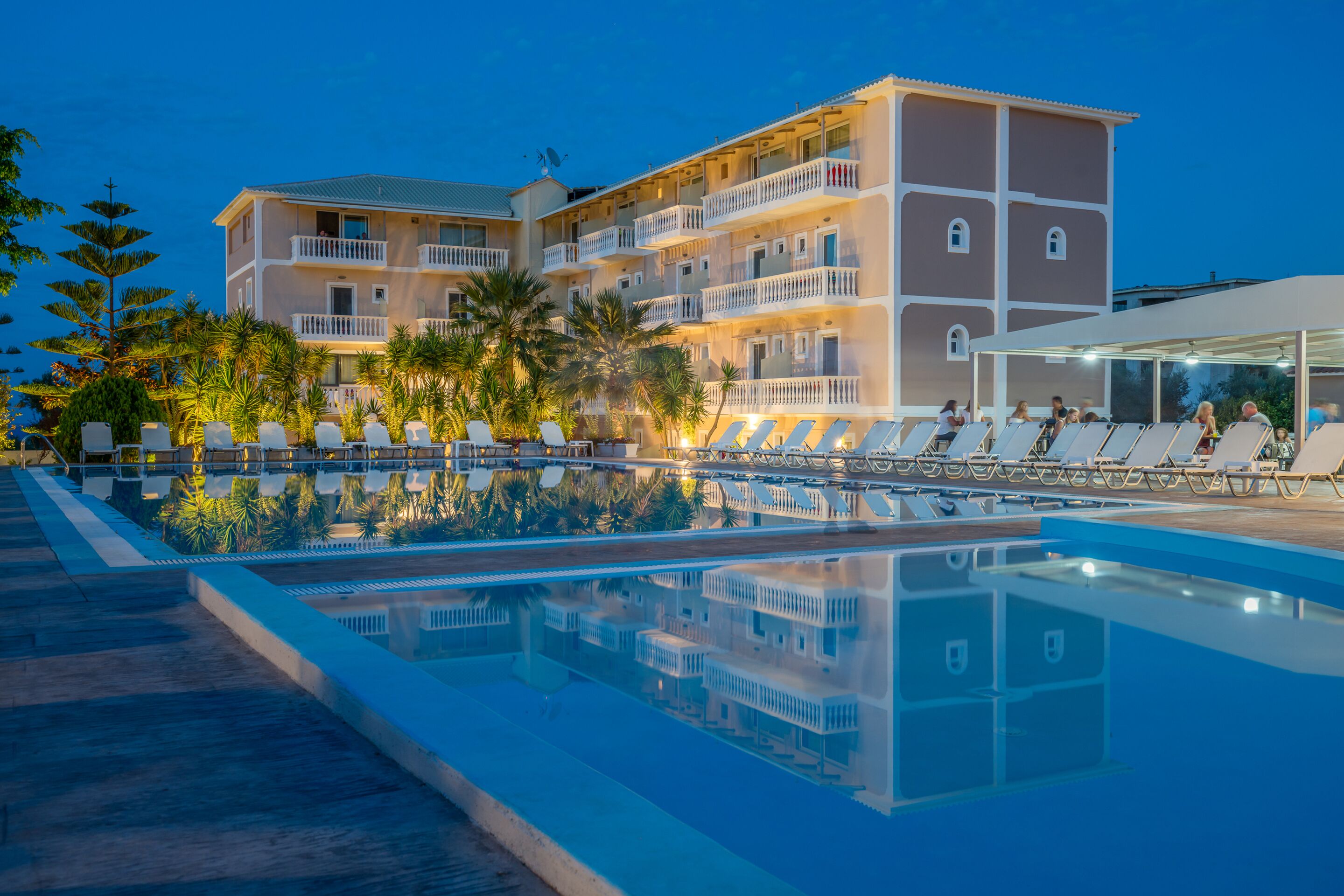 Een hotel met een zwembad, meerdere balkons en palmbomen.