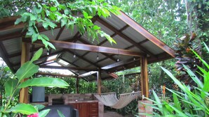 A covered outdoor kitchen area with a hammock, surrounded by lush greenery and plants. - San Gabriel Apartments (La Fortuna)
