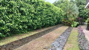 A stone pathway bordered by a hedge and a row of purple-leaved plants. - San Gabriel Apartments (La Fortuna)