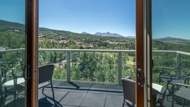 Un balcon donnant sur un paysage montagneux, avec des fauteuils en osier et une porte vitrée.