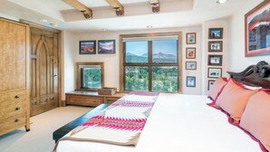 A bedroom with a large bed, a wooden wardrobe, a television, and a window with a mountain view. - Penthouse At The Peaks 744 (Mountain Village)