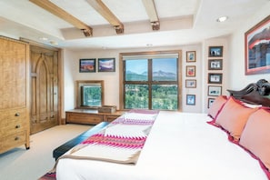 Une chambre à coucher avec un grand lit, une armoire en bois, une télévision et une fenêtre donnant sur la montagne.