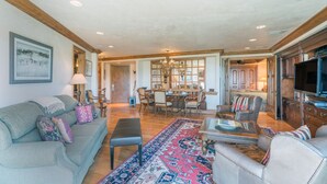 Un salon spacieux avec un grand canapé, une table basse et un tapis à motifs. On y trouve également un coin repas agrémenté d’un lustre et de meubles en bois.