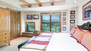 Une chambre avec un grand lit, une armoire en bois, une fenêtre donnant sur la montagne et des tableaux encadrés accrochés au mur.