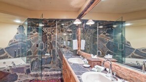 A bathroom with a stone wall design, a long vanity with two sinks, and a large mirror. - Penthouse At The Peaks 614 (Mountain Village)
