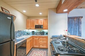 A compact kitchen with wooden cabinets, a black refrigerator, a microwave, a stove, and a coffee maker. - Penthouse At The Peaks 614 (Mountain Village)