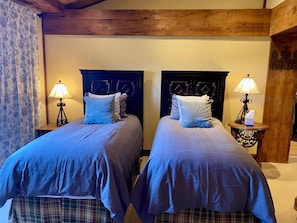 A room with two beds, each with a headboard, a bedside table with a lamp, and a floral curtain. - Penthouse At The Peaks 614 (Mountain Village)