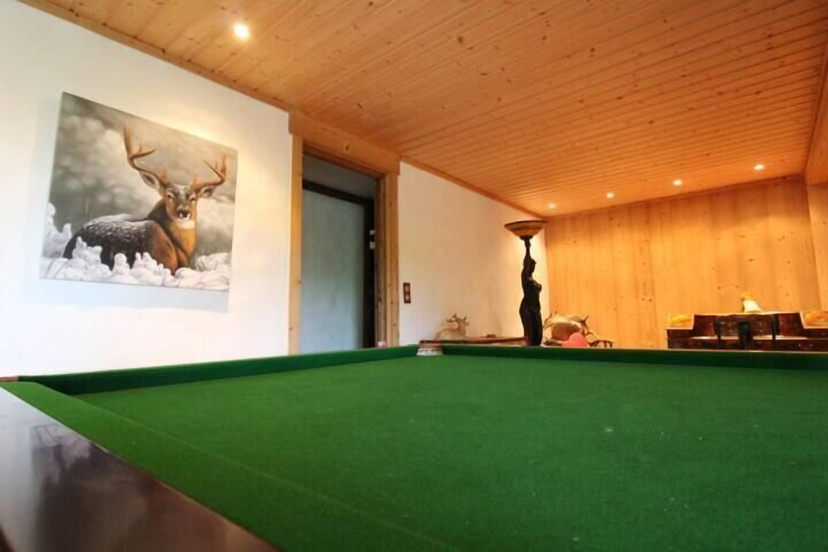 A pool table in a room with wooden ceiling and walls, a painting of a deer, and a person playing pool.