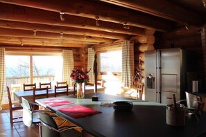 A wooden cabin interior with a dining table, chairs, a refrigerator, and a window with curtains. - Chalet Marmotte, 400m2 of comfort (Font-Romeu)
