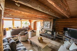 A log cabin interior with a fireplace, sofa, television, and a dining area.