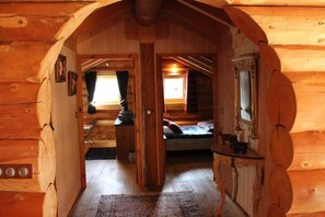 A log cabin interior with a cozy bedroom, a small sitting area, and a dining table.