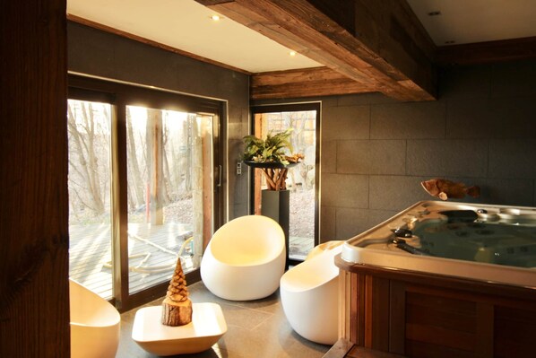 A modern spa room with a hot tub, wooden accents, and large windows offering a view of the outdoors.