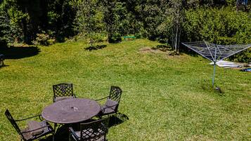 A grassy outdoor area with a round table and four chairs, surrounded by trees and a hammock.