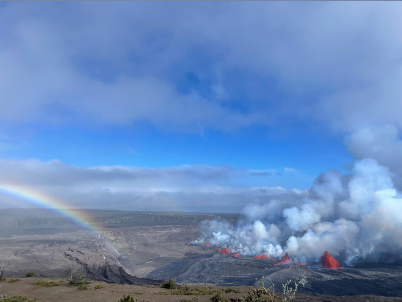 A volcanic landscape with a rainbow, steam, and smoke.