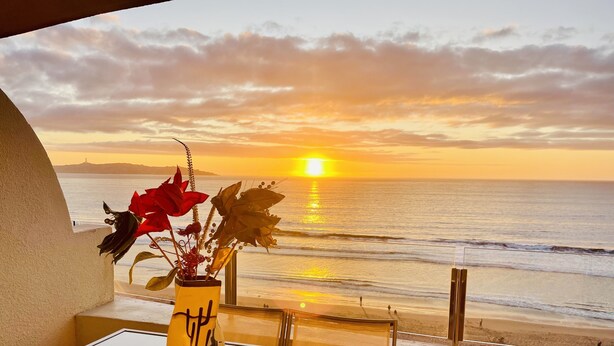 A balcony with a view of the ocean at sunset, a vase with flowers, and a table. - La Serena Vacations, Chile! (La Serena)