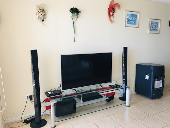 A living room with a flat-screen TV, two speakers, a glass coffee table, and a small black speaker.