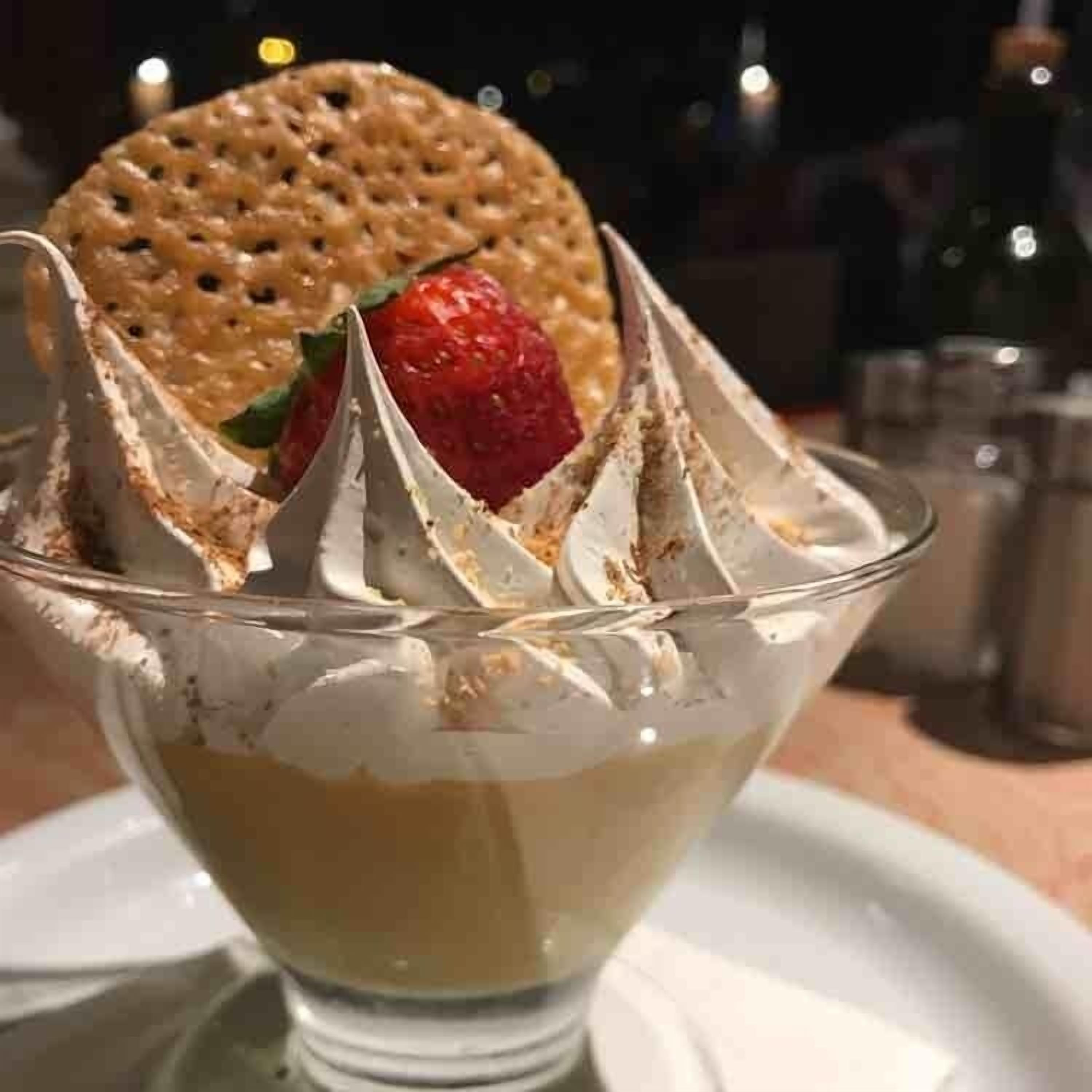 Un dessert in una ciotola di vetro trasparente, con panna montata e una fragola sopra.