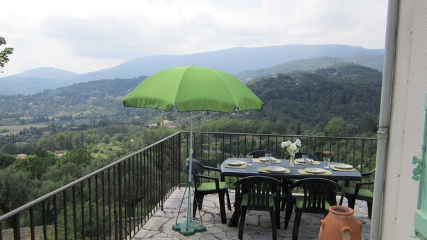 Una terrazza con un tavolo apparecchiato per mangiare, un ombrellone verde e vista sul paesaggio circostante.