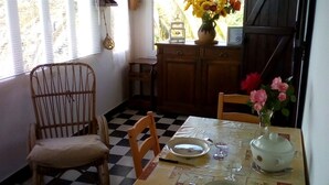 Zona pranzo con pavimento a scacchi, sedie di legno, tavolo apparecchiato con piatti, bicchieri e un vaso con fiori.
