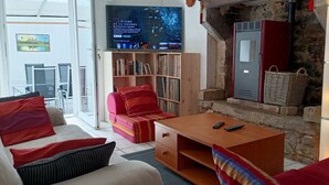 A cozy living room with a sofa, a coffee table, and a bookshelf. There is a television mounted on the wall displaying a program. - Between Quimper and Douarnenez, 10 minutes from the beach (Plogastel-Saint-Germain)