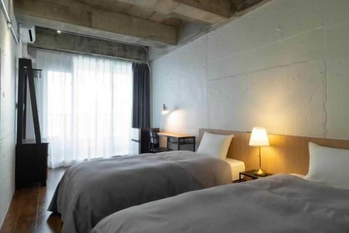 A hotel room with two beds, a desk, a chair, and a window with curtains.