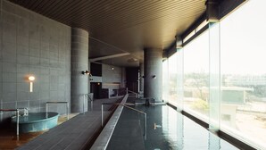 Un área de piscina interior moderna con una piscina larga y estrecha, paredes de azulejos y grandes ventanales que ofrecen vistas al exterior.