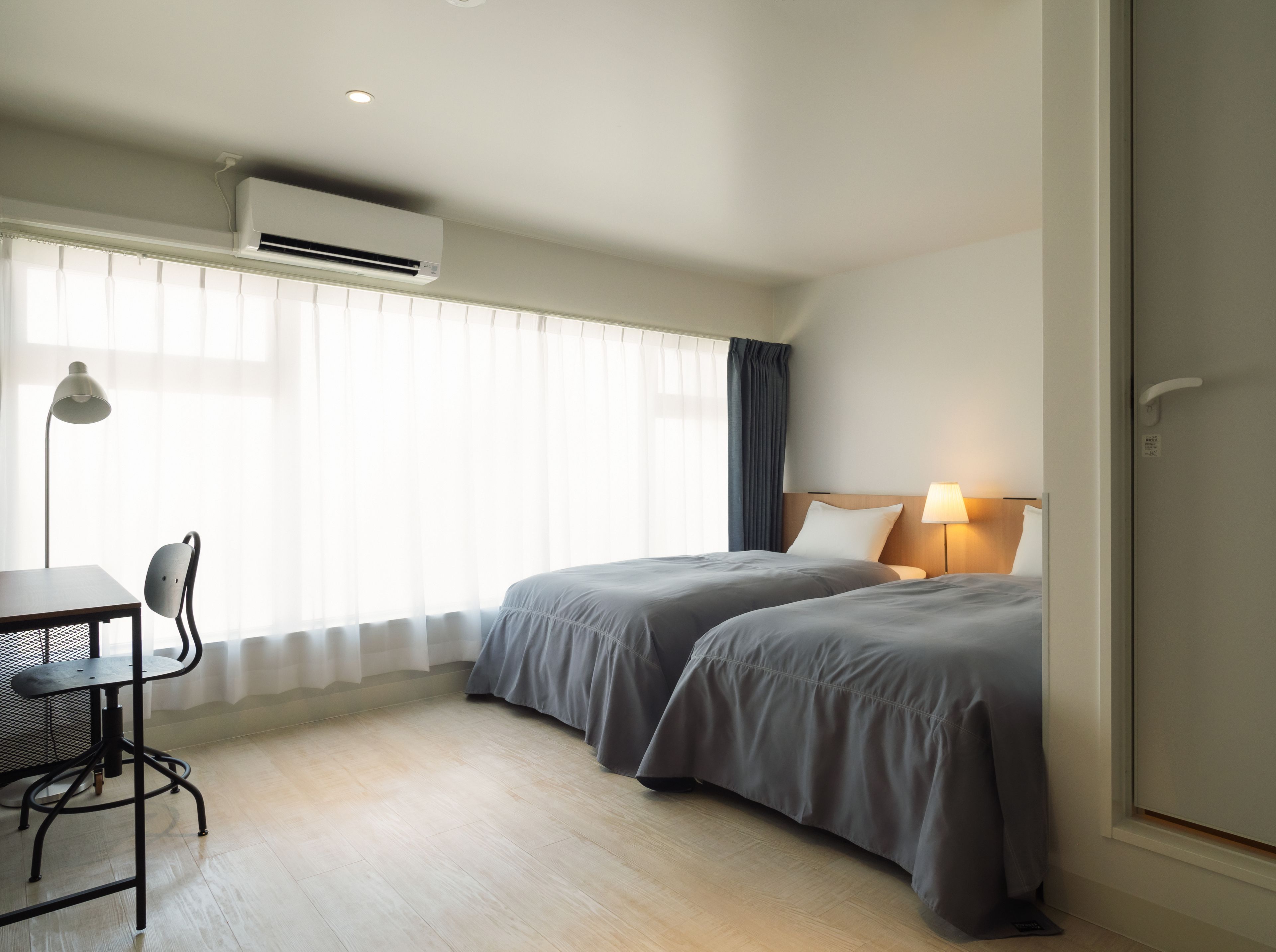 Une chambre d’hôtel avec deux lits, un bureau, une chaise et une lampe.