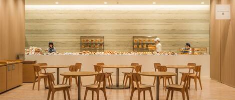 A bakery cafe with wooden tables and chairs, a marble wall, and a display case with baked goods.