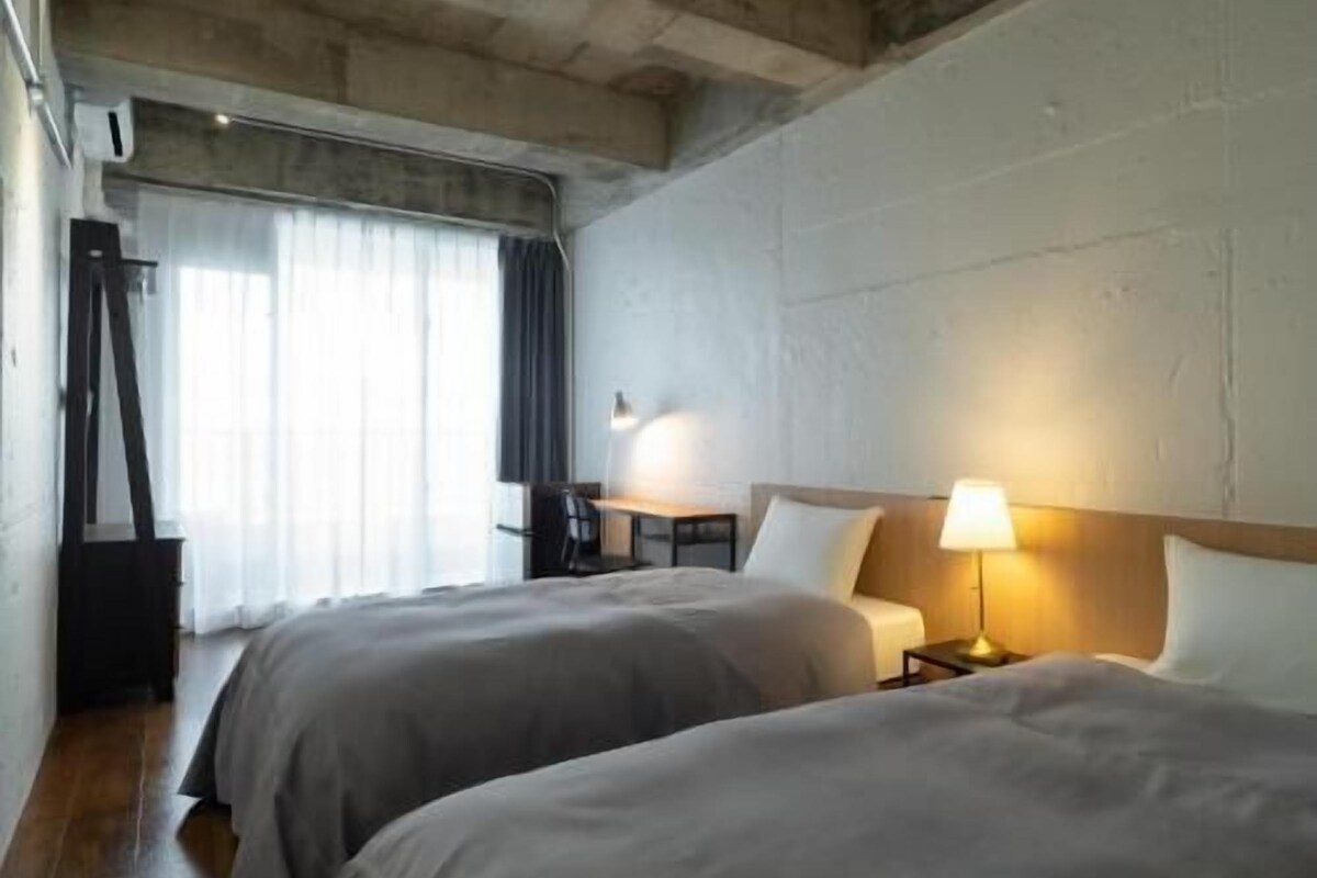 A hotel room with two beds, a desk, a chair, and a window with curtains.