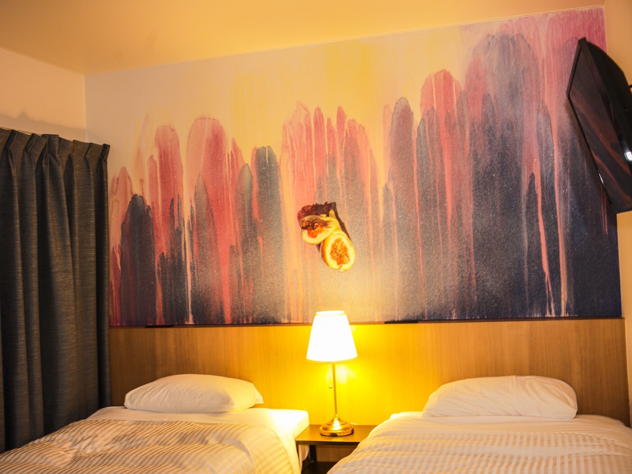 Una camera d'albergo con due letti, un grande quadro astratto appeso alla parete e una lampada sul comodino.