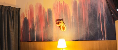 A hotel room with two beds, a large abstract painting on the wall, and a lamp on the nightstand.