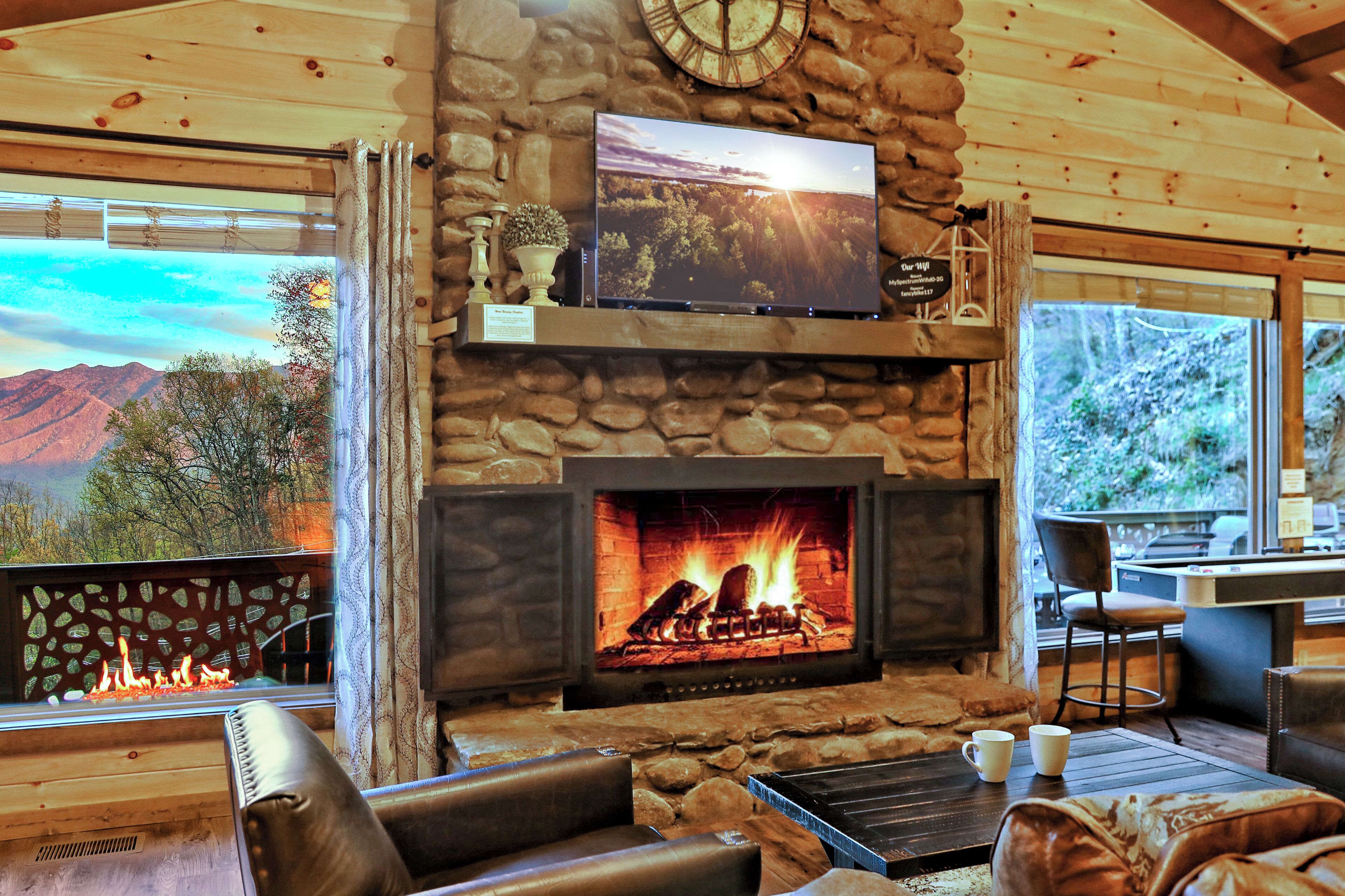 A stone fireplace with a TV above it, a comfortable seating area with a view of the mountains through the window.