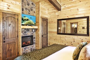 Habitación tipo cabaña de madera con chimenea de piedra, un televisor y un espejo grande en la pared.