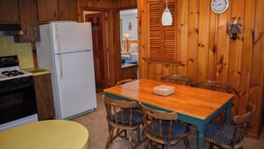 Una cuina amb armaris de fusta, un refrigerador blanc, una cuina i una taula de dinar amb cadires.