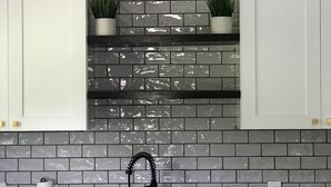 A kitchen with grey tiled backsplash, white cabinets, and two potted plants on a shelf. - Charming Heights Guesthouse! (Houston)