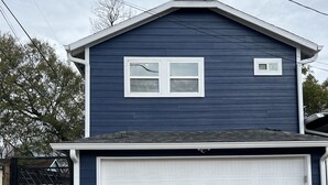 A two-story house with a garage, a fenced yard, and a brick driveway. - Charming Heights Guesthouse! (Houston)