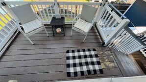 A wooden deck with two wicker chairs and a small table, a checkered rug, and a view of a backyard with a house and a fence. - Charming Heights Guesthouse! (Houston)