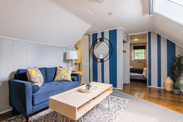 A modern living room with a blue sofa, a wooden coffee table, and a patterned rug. - Charming Hideaway in Westport | 16 (KCMO)