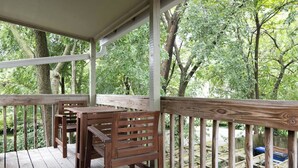 Um deck de madeira com bancos e guarda-corpo, rodeado por árvores.