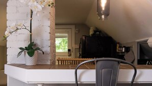 Uma cozinha com parede de tijolos brancos, luminária pendente e uma orquídea em vaso.
