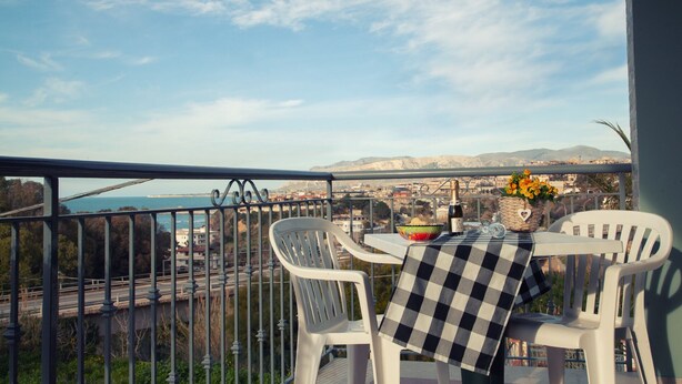 A balcony with a table set for two, overlooking a coastal cityscape.