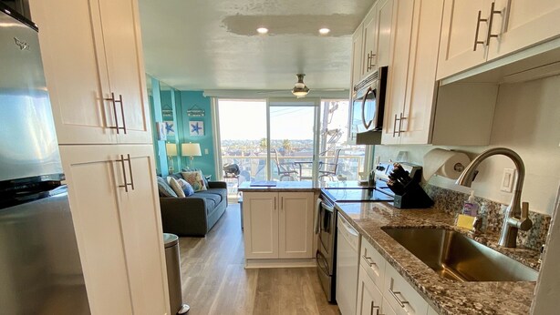 A modern kitchen with white cabinets, a granite countertop, and a stainless steel sink. - Find your beach bliss! (San Diego)