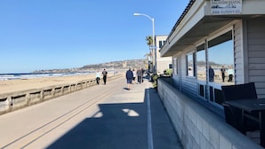 A coastal walkway with a beach view, a sign for a vacation rental, and a building with large windows. - Find your beach bliss! (San Diego)
