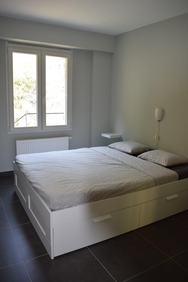 Quarto com cama, janela, mesa de cabeceira e luminária na parede.