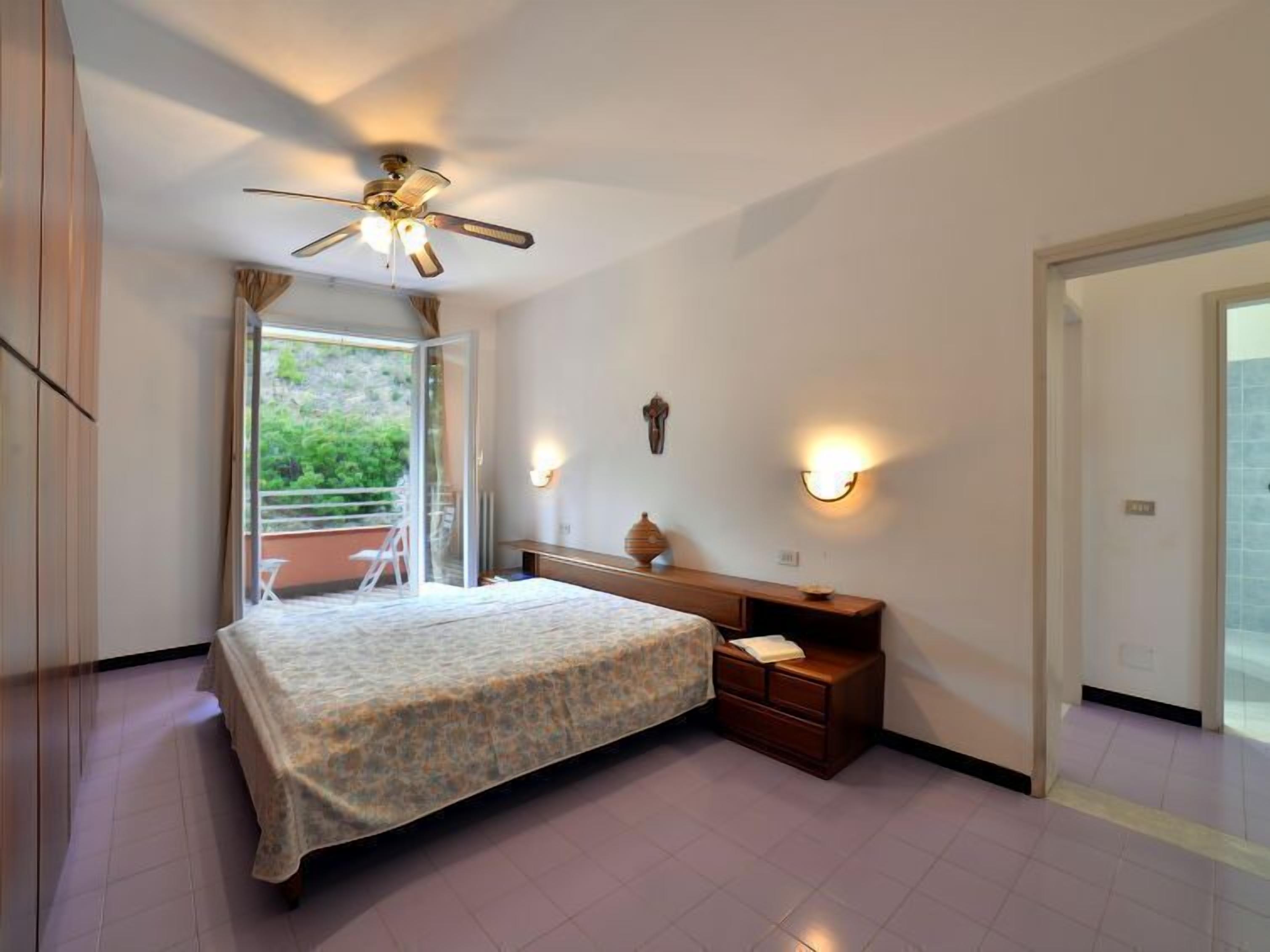 A bedroom with a bed, bedside table, wall-mounted lamp, and a ceiling fan.