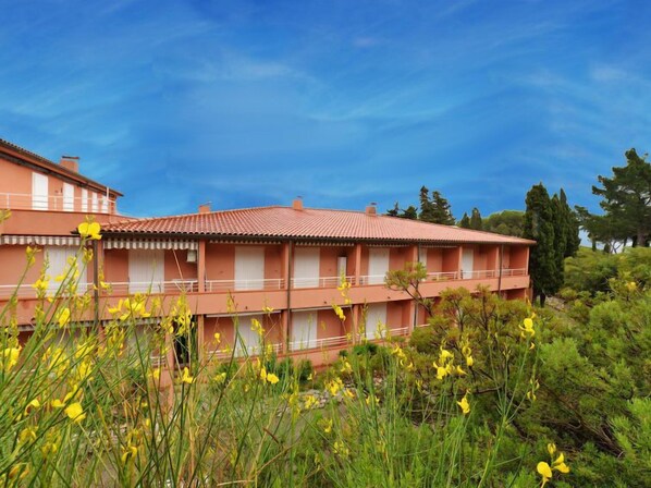 A two-story building with a red-tiled roof, balconies, and a garden with yellow flowers. - Mimose 2 by Interhome (Rio Marina)